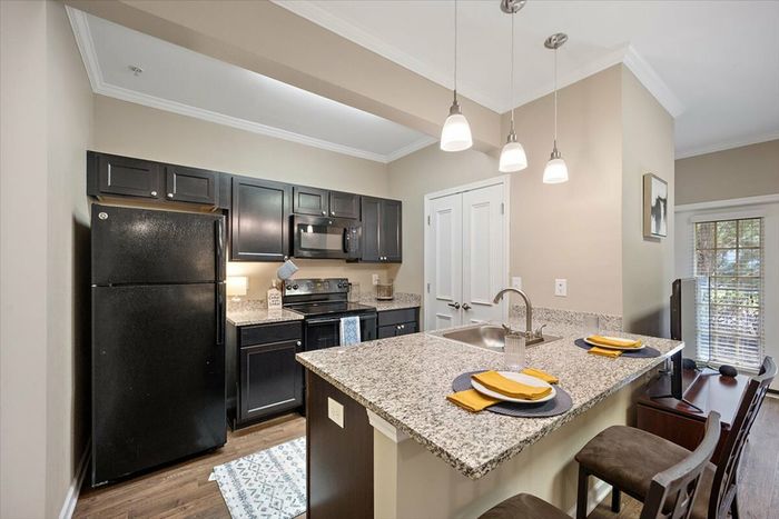 Modern kitchen at Eagle Flatts Apartments in Hattiesburg, MS featuring granite countertops and black appliances.