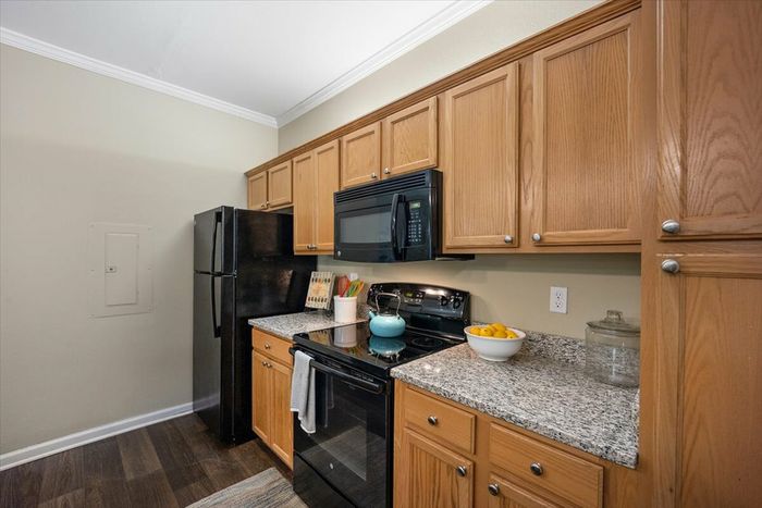 Modern kitchen at Eagle Flatts Apartments in Hattiesburg, MS with granite countertops, black appliances, and wood cabinetry.