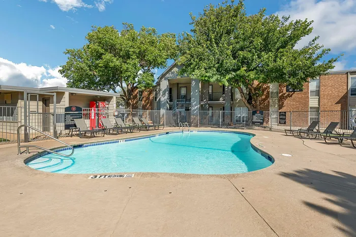Community pool with sun chairs in front of apartments