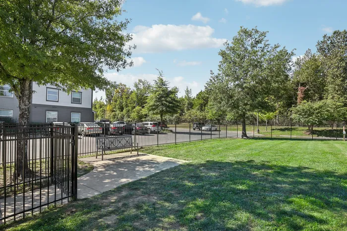 Fenced pet park and outdoor grassy area with trees and nearby apartment buildings at The Preserve Murfreesboro, ideal for pet-friendly activities or outdoor relaxation.