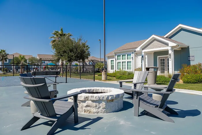 Inviting outdoor patio with cozy fire pit and modern seating, adjacent to a stylish clubhouse and lush greenery.