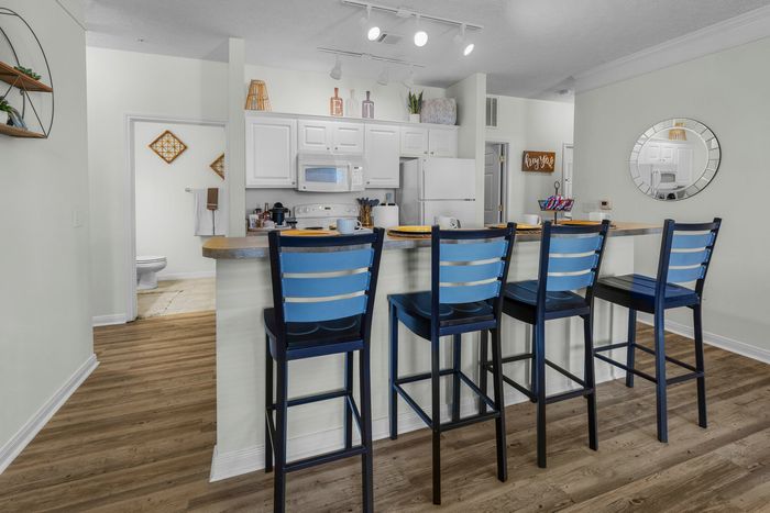 Charming kitchen with a cozy breakfast bar, featuring contemporary bar stools, sleek white cabinetry, and warm wooden flooring.