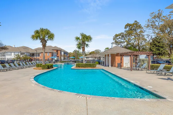 Inviting outdoor pool area with lounge chairs, palm trees, and a stylish poolside cabana at a modern apartment complex.