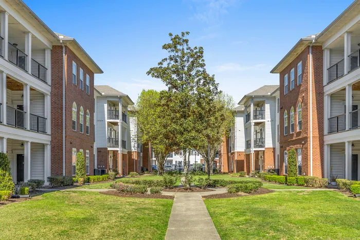 Charming apartment complex with brick facades and lush green courtyard, offering a serene and inviting community atmosphere.