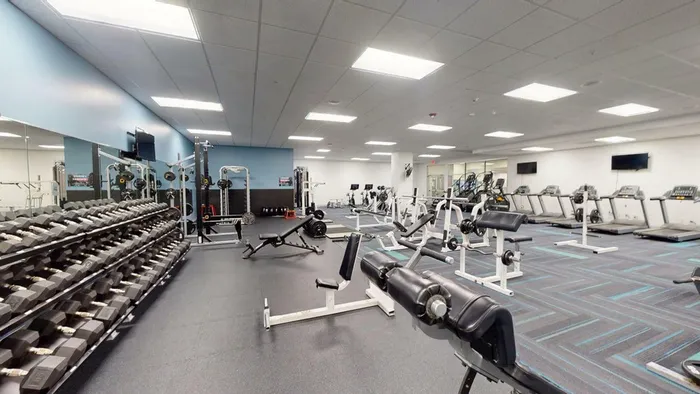 Expansive fitness center with state-of-the-art gym equipment, including treadmills, free weights, and weight machines in a modern, well-lit space.