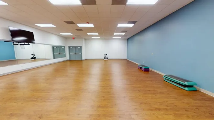 Spacious fitness studio with polished hardwood floors, mirrored wall, and vibrant blue accent wall, perfect for yoga or aerobics classes.