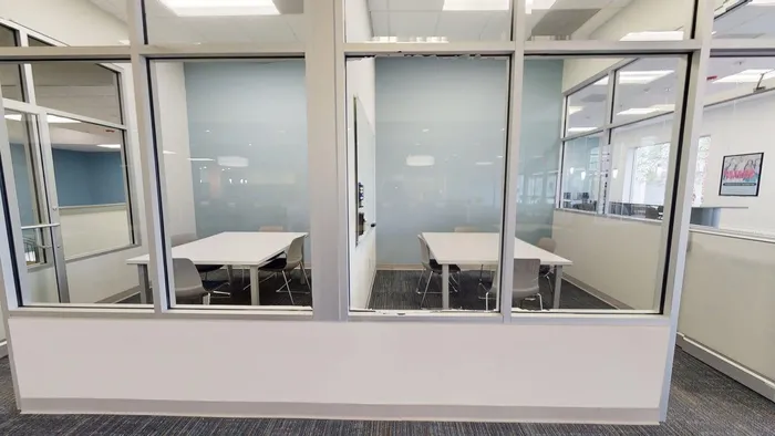 Modern office space featuring glass-enclosed meeting rooms with sleek furnishings and neutral decor.