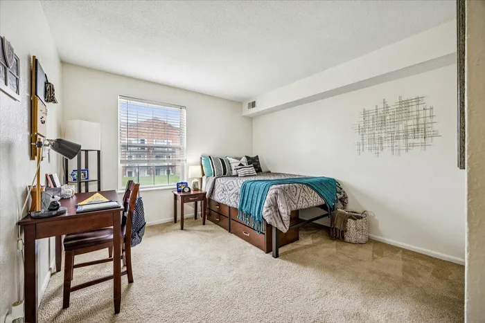 Inviting bedroom with cozy bed, stylish desk, and natural light from large window, perfect for comfort and productivity.