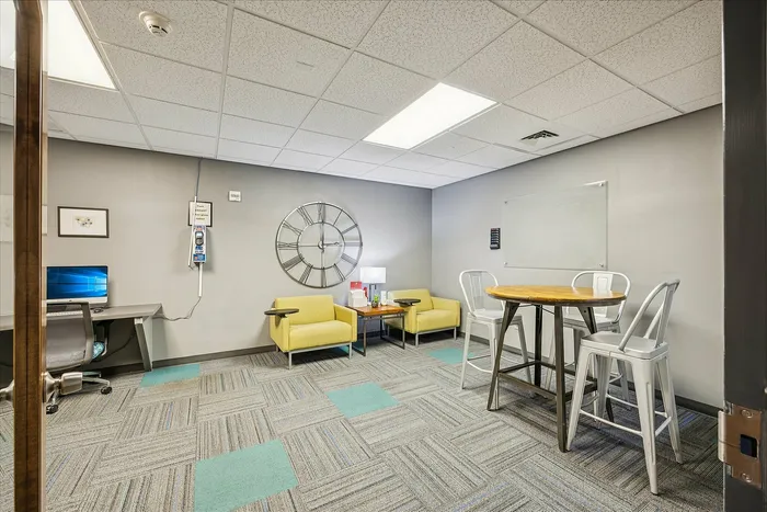 Modern workspace featuring a cozy seating area with yellow chairs, a stylish round table with metal chairs, and a large decorative wall clock.