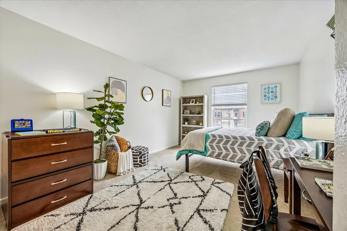 Inviting bedroom with stylish decor, featuring a cozy bed with geometric bedding, a chic dresser with modern lamp, and elegant wall art.