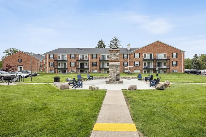 Inviting apartment complex featuring red brick buildings, spacious balconies, and a charming outdoor seating area surrounded by lush greenery.