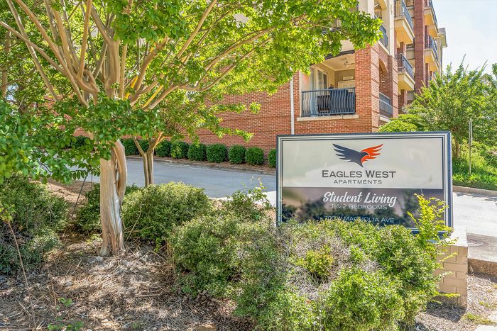 Inviting exterior of Eagles West Apartments with lush greenery and modern brick architecture, ideal for student living with 1 & 2 bedroom options.