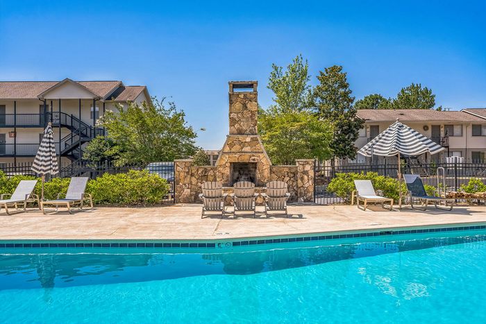 Inviting outdoor pool area with comfortable loungers, a charming stone fireplace, and vibrant greenery, perfect for relaxation and leisure.