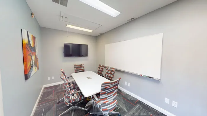 Contemporary meeting room featuring a sleek conference table, vibrant chairs, wall-mounted TV, and spacious whiteboard, ideal for productive gatherings.