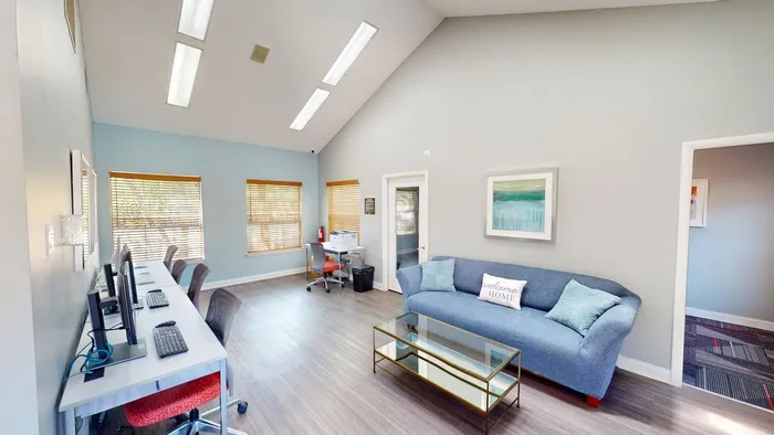 Bright and welcoming community room featuring modern computer workstations, cozy seating, and natural light through large windows.