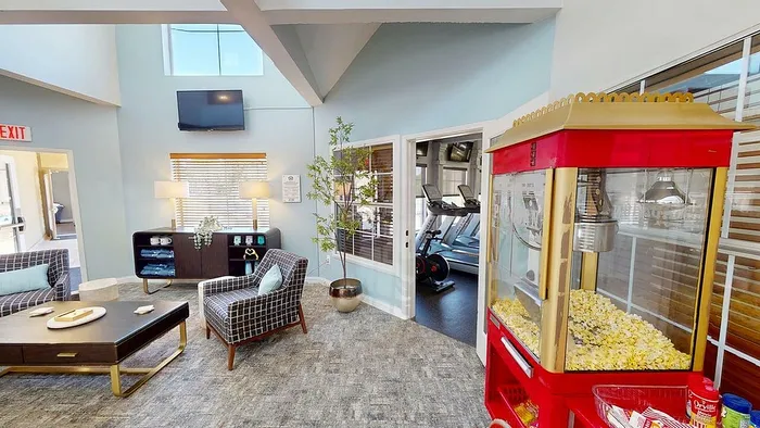 Bright lounge area with modern seating and a popcorn machine, adjacent to a state-of-the-art fitness center, perfect for relaxation and wellness.