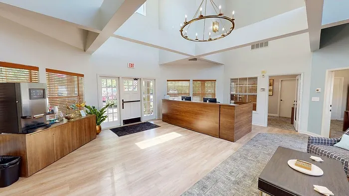 Elegant open-concept apartment lobby featuring a modern wooden reception desk, stylish chandelier, and natural light streaming through large windows.