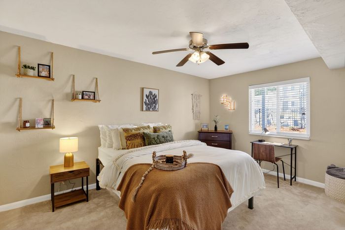 Inviting bedroom with cozy decor, featuring a plush bed, chic wall shelves, and ample natural light through a large window.