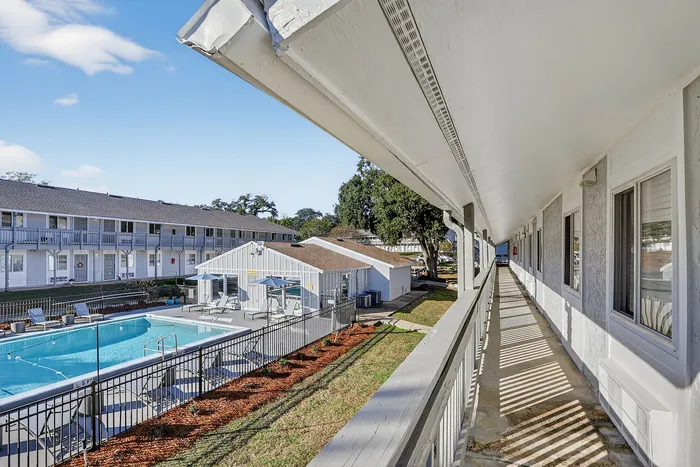 Charming apartment building exterior with a glistening pool and sunlit walkways, ideal for relaxed living.