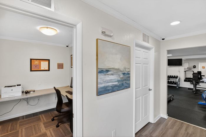 Inviting hallway view leading to a home office with modern desk setup and elegant decor, adjacent to a well-equipped home gym.