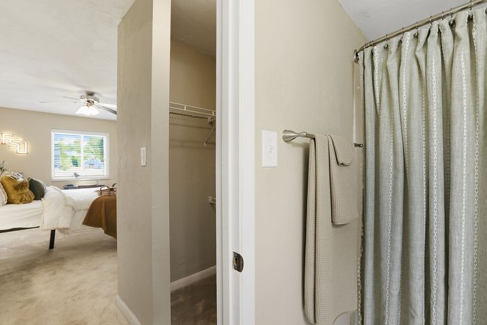 Inviting bedroom with plush bedding and a cozy walk-in closet next to a stylish bathroom featuring modern curtains.