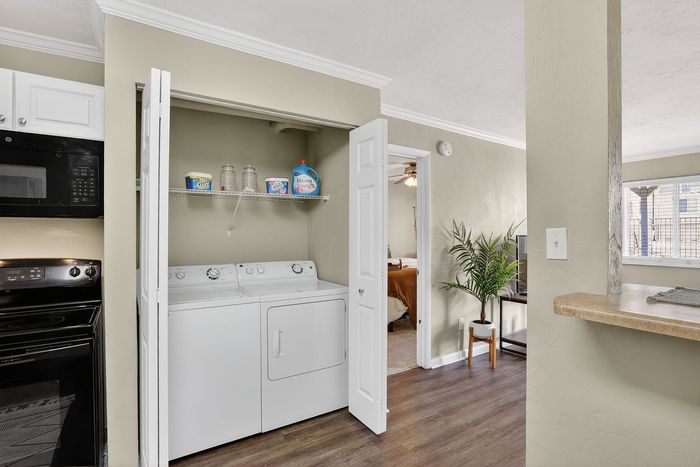 Inviting apartment interior featuring a sleek laundry area with washer and dryer, adjacent to a cozy living space and bedroom. Modern convenience meets stylish design.