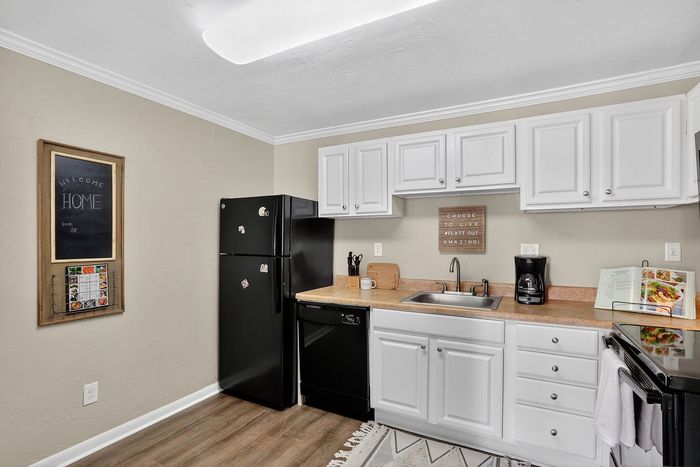 Charming kitchen with sleek black appliances, elegant white cabinetry, and natural wood flooring offers a warm and inviting atmosphere.
