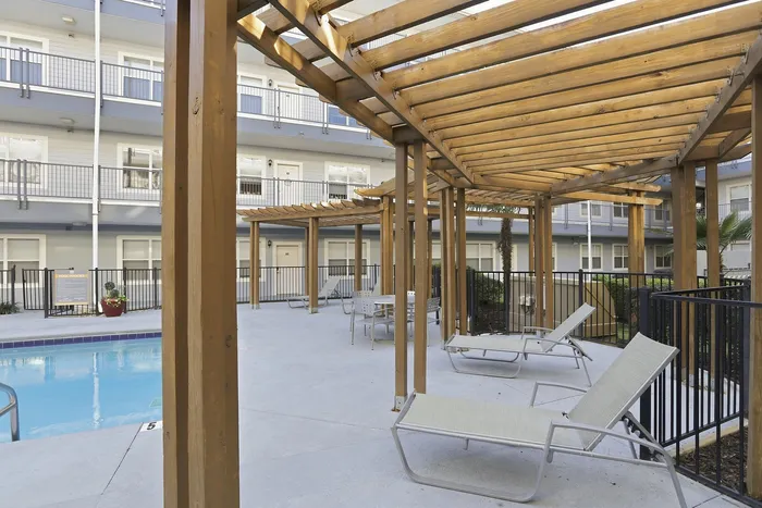 Modern apartment complex with a luxurious pool area featuring wooden pergolas and comfortable loungers, creating a serene outdoor retreat.
