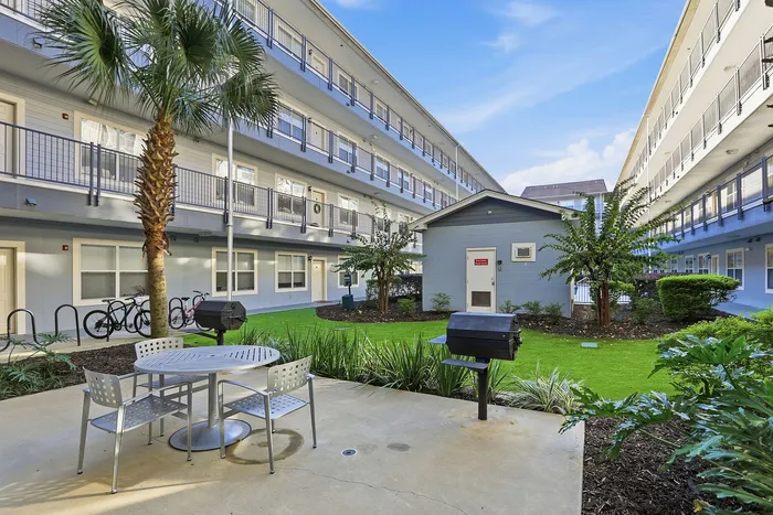 Charming apartment courtyard featuring lush greenery, outdoor seating, and barbecue grills, perfect for relaxation and social gatherings.