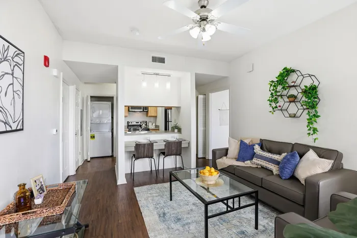 Chic and modern living room featuring a cozy sofa with plush pillows, stylish glass coffee table, and lush greenery on the walls, perfect for relaxation and comfort.