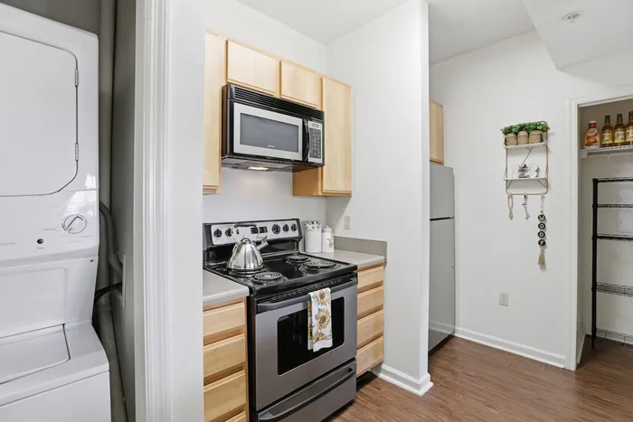 Charming apartment kitchen featuring modern appliances, sleek wooden cabinetry, and an in-unit washer and dryer combo.