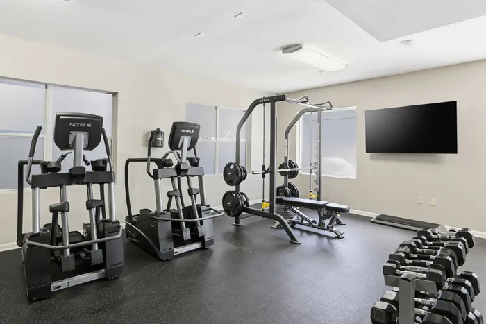 Modern apartment fitness center equipped with advanced cardio machines, weight bench, and flat-screen TV for a comprehensive workout experience.