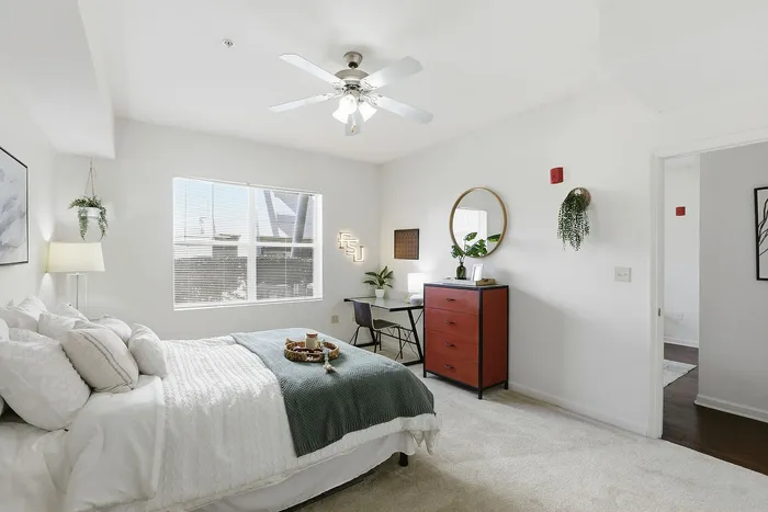 Bright, stylish bedroom with cozy bed, elegant desk, and chic decor, featuring ample natural light and plush carpeting.