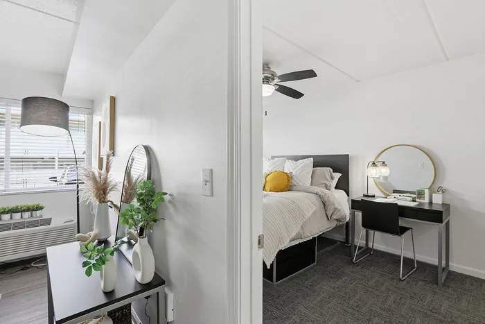 Bright, modern bedroom with cozy decor, featuring a stylish workspace and elegant plant accents for a serene living experience.