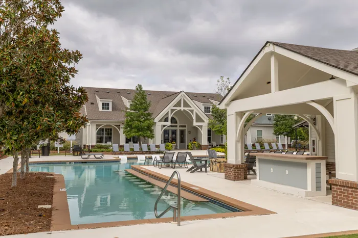 Charming apartment complex featuring a pristine outdoor pool, inviting lounge chairs, and elegant architecture surrounded by lush greenery.
