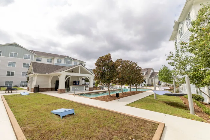 Contemporary apartment community with inviting pool, lush green spaces, and relaxing hammocks under a cloudy sky.