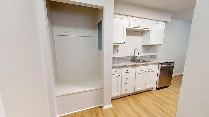 Modern kitchen with sleek granite countertops, stainless steel dishwasher, and ample white cabinetry, complemented by elegant wood flooring.