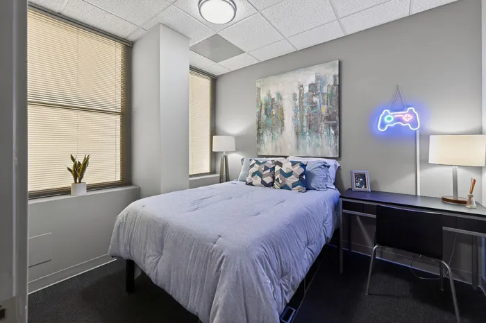 Modern bedroom with cozy gray bedding, artistic wall decor, and neon gamer sign for a unique touch.