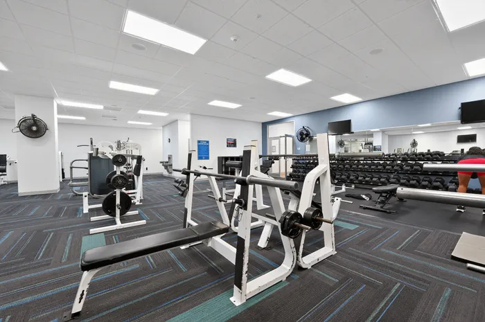 Spacious and modern gym with weightlifting equipment, sleek flooring, and ample lighting for an invigorating workout experience.