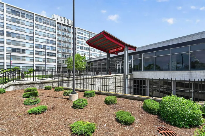 Contemporary apartment building with expansive windows, lush landscaping, and a welcoming entrance at University Plaza.