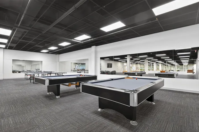 Expansive recreational room featuring multiple sleek billiard tables, modern lighting, and mirrored walls for a luxurious gaming experience.