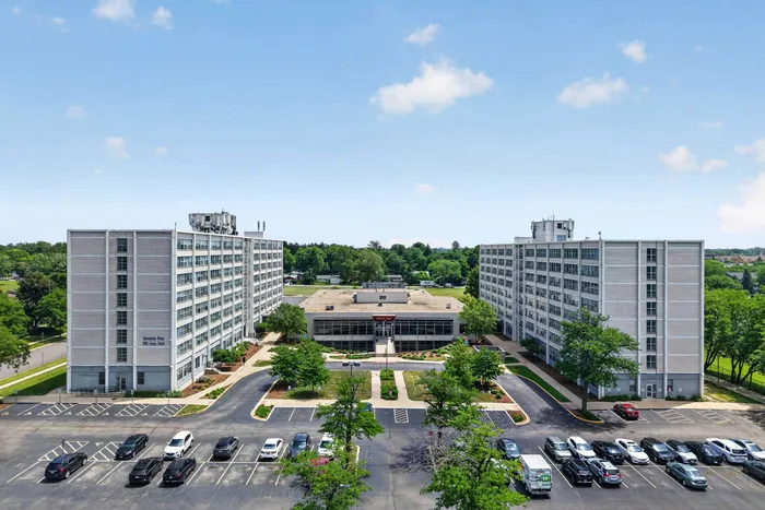 Impressive aerial view of modern apartment complex with twin high-rise buildings and lush greenery, ample parking space, and inviting pathways.