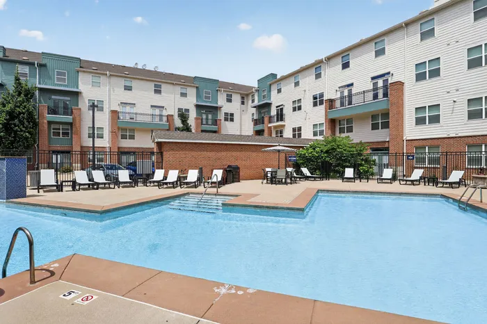 Inviting apartment complex with modern architecture, featuring a spacious swimming pool and stylish lounge area surrounded by comfortable sunbeds.