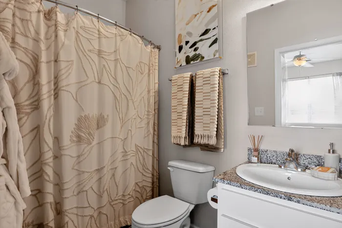 Charming bathroom with elegant floral shower curtain, chic granite countertop, and beautifully folded towels for a cozy atmosphere.