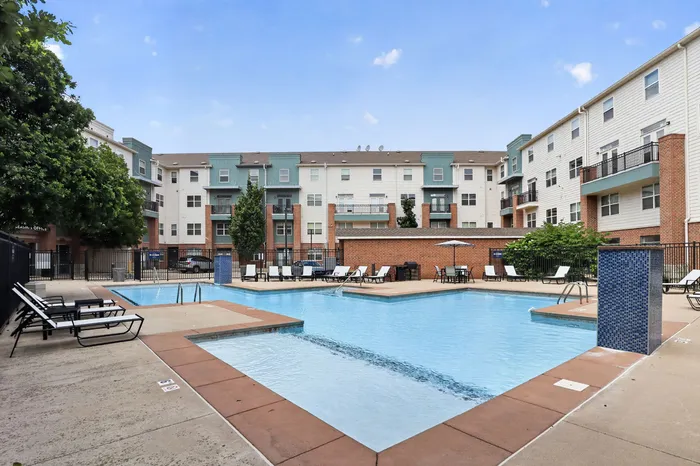 Inviting apartment complex with luxurious pool, surrounded by stylish lounge chairs and vibrant greenery.