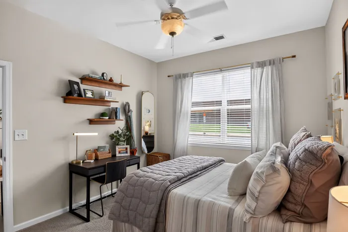 Cozy bedroom with stylish decor, plush bedding, and a modern workspace bathed in natural light.