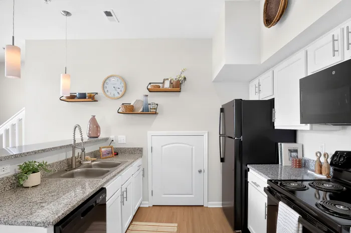 Modern kitchen with granite countertops, sleek black appliances, and stylish open shelving, perfect for culinary creativity.