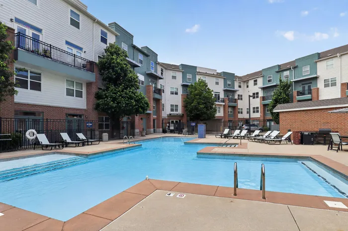 Modern apartment complex with a spacious swimming pool, poolside lounge chairs, and lush landscaping, offering a perfect blend of relaxation and style.
