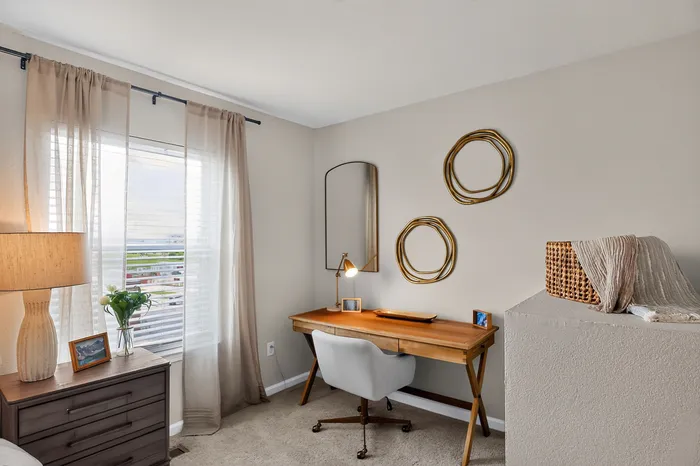 Bright and cozy home office featuring a sleek wooden desk, stylish decor, and a large window with sheer curtains.
