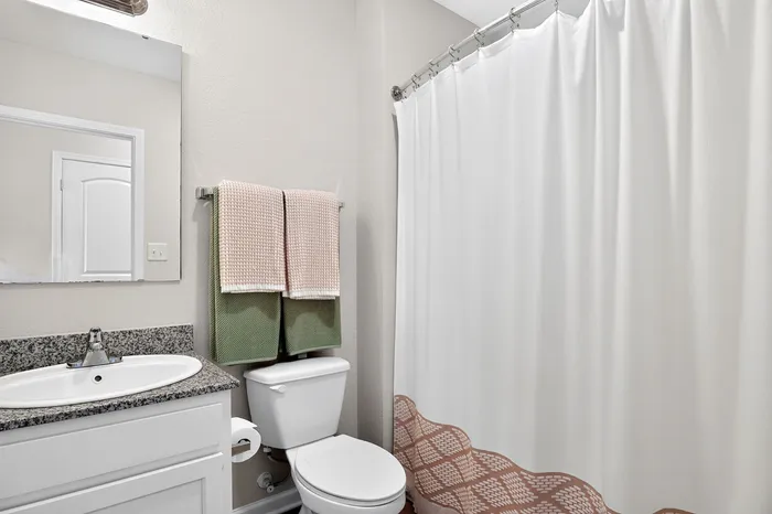 Modern bathroom featuring a sleek granite countertop, elegant sink, and cozy neutral decor with matching plush towels and a clean white shower curtain.